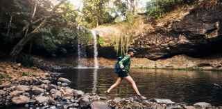 Image of woman walking over rocks near waterfall